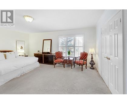 A white bedroom with a bed, dresser, chair, and mirror.
