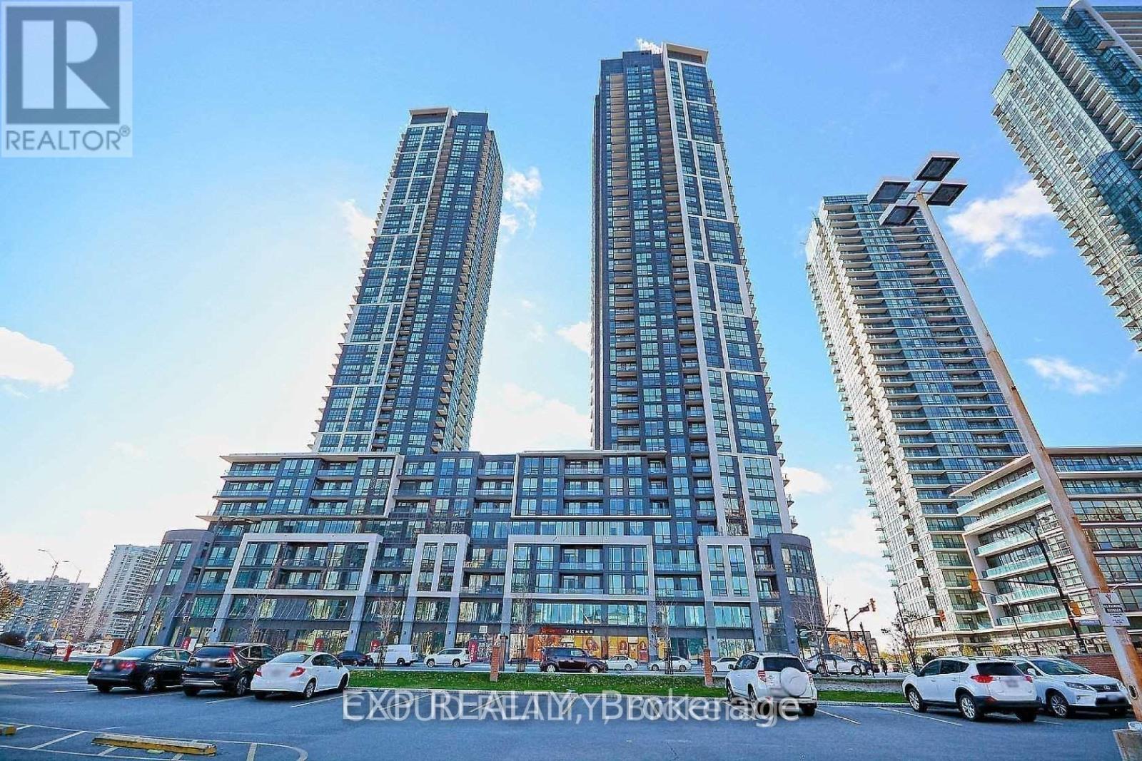 A tall building with a glass facade stands in front of other buildings.