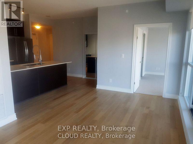 A room with wooden flooring and a kitchen area with a sink and cabinets.