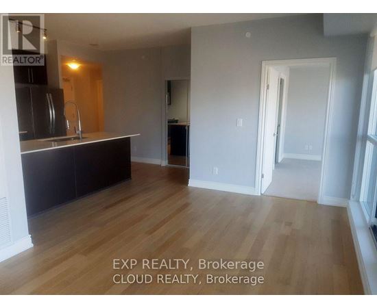A room with wooden flooring and a kitchen area with a sink and cabinets.