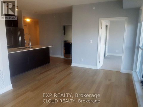 A room with wooden flooring and a kitchen area with a sink and cabinets.