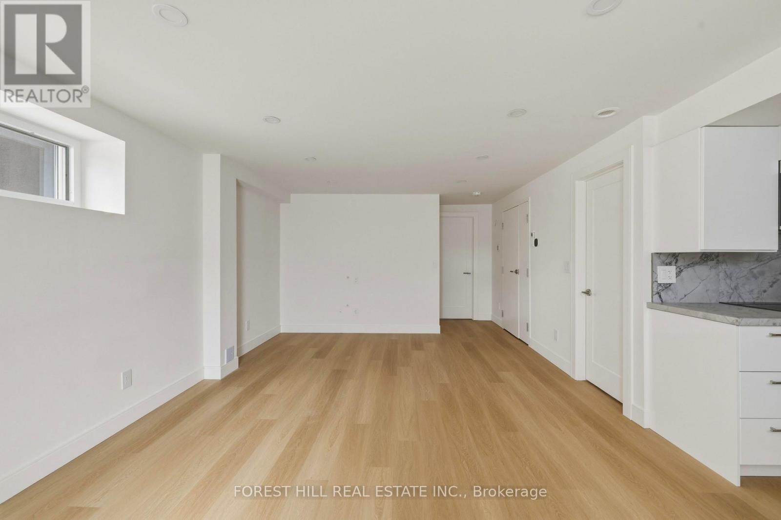 A spacious room with wooden flooring and white walls, part of a real estate listing.