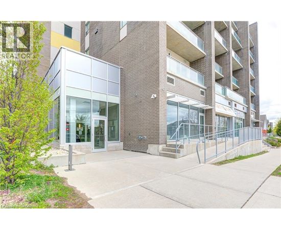 A modern building with glass doors and windows is surrounded by a sidewalk and a metal fence.