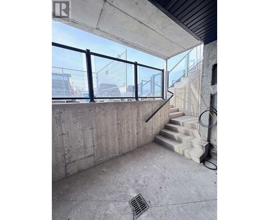 A concrete room with a staircase and a window overlooking a construction site.
