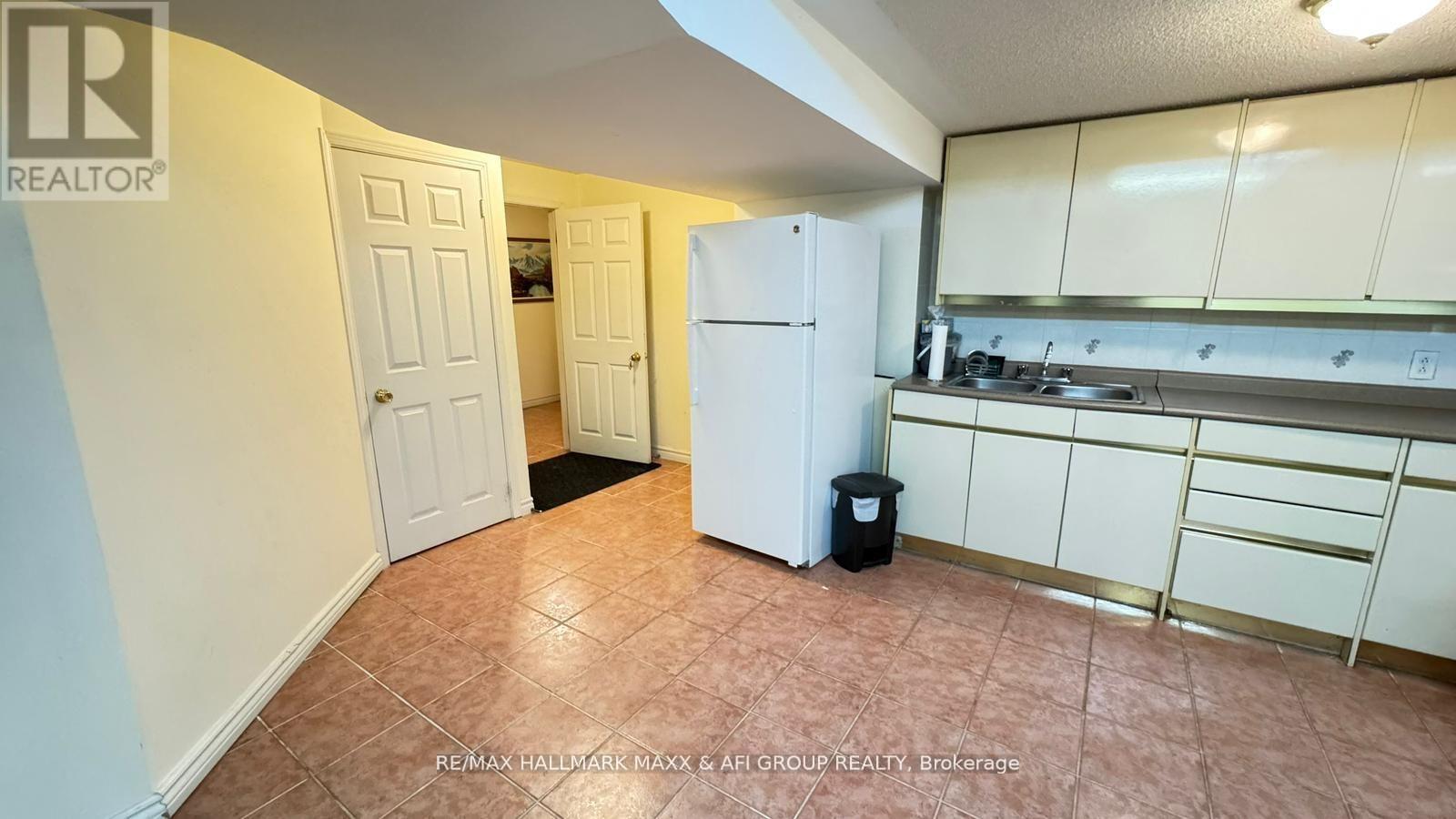 A kitchen area with a refrigerator, cabinets, and a trash can.
