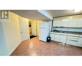 A kitchen area with a refrigerator, cabinets, and a trash can.
