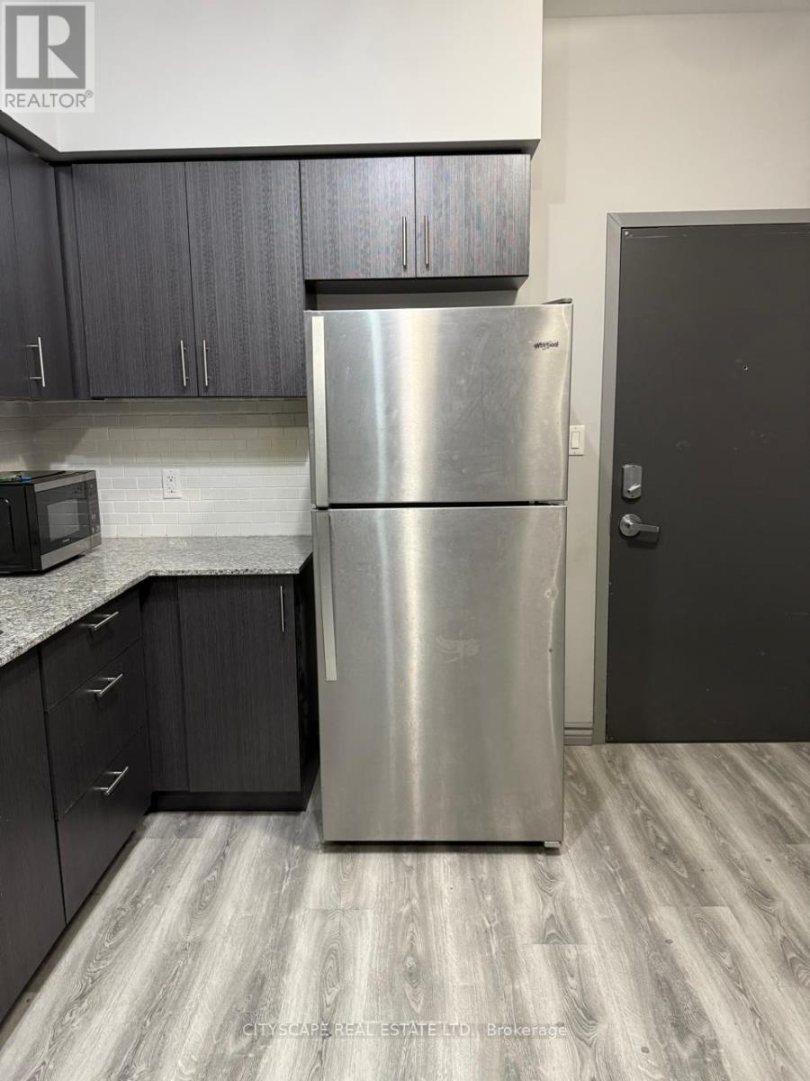 A stainless steel refrigerator stands in a kitchen with dark wood cabinets.