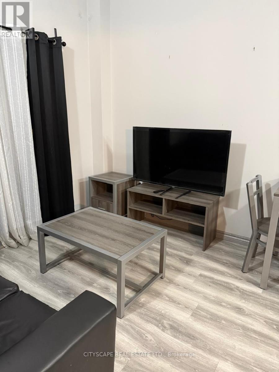 A black television is on a wooden stand in a room with a grey floor.