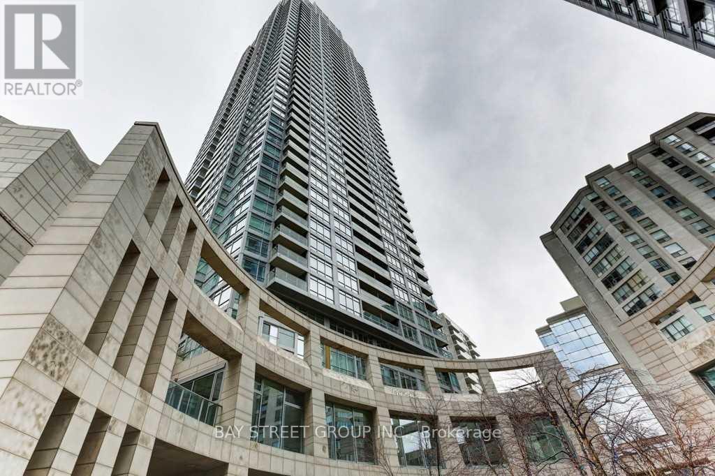 A tall building with a glass facade stands in front of a building with a stone facade.