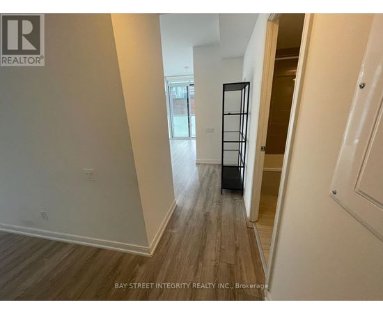 A hallway with wood flooring and white walls, leading to a door with a black frame.