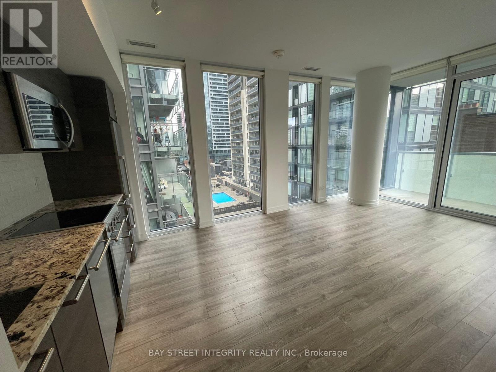 A spacious room with wooden flooring and large windows overlooking a cityscape.