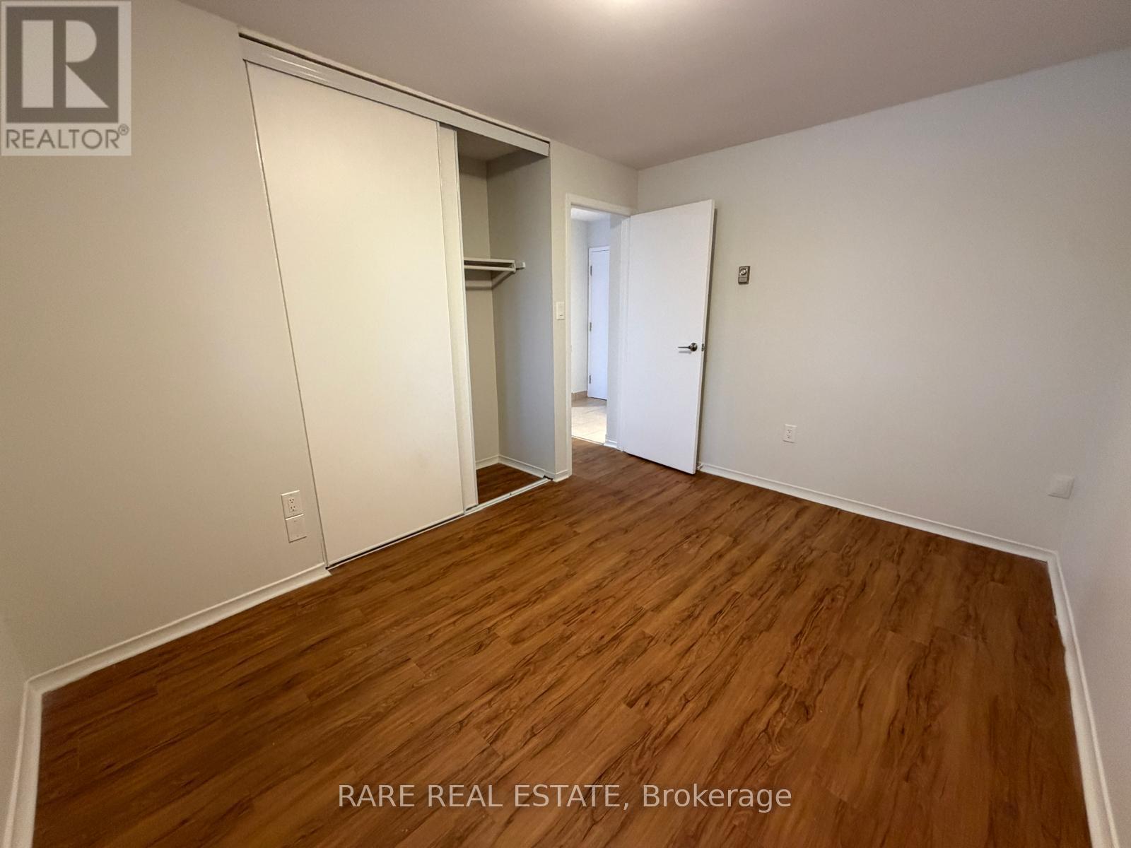 A room with wooden flooring and white walls, with a door on the right and a closet on the left.