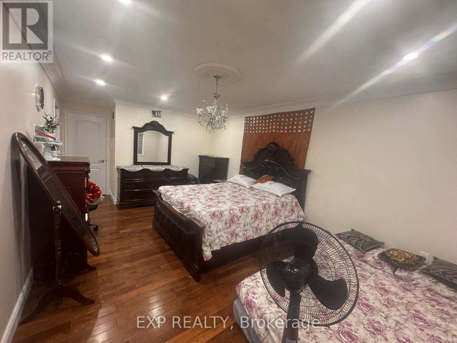 A bedroom with a bed, dresser, mirror, and chandelier.