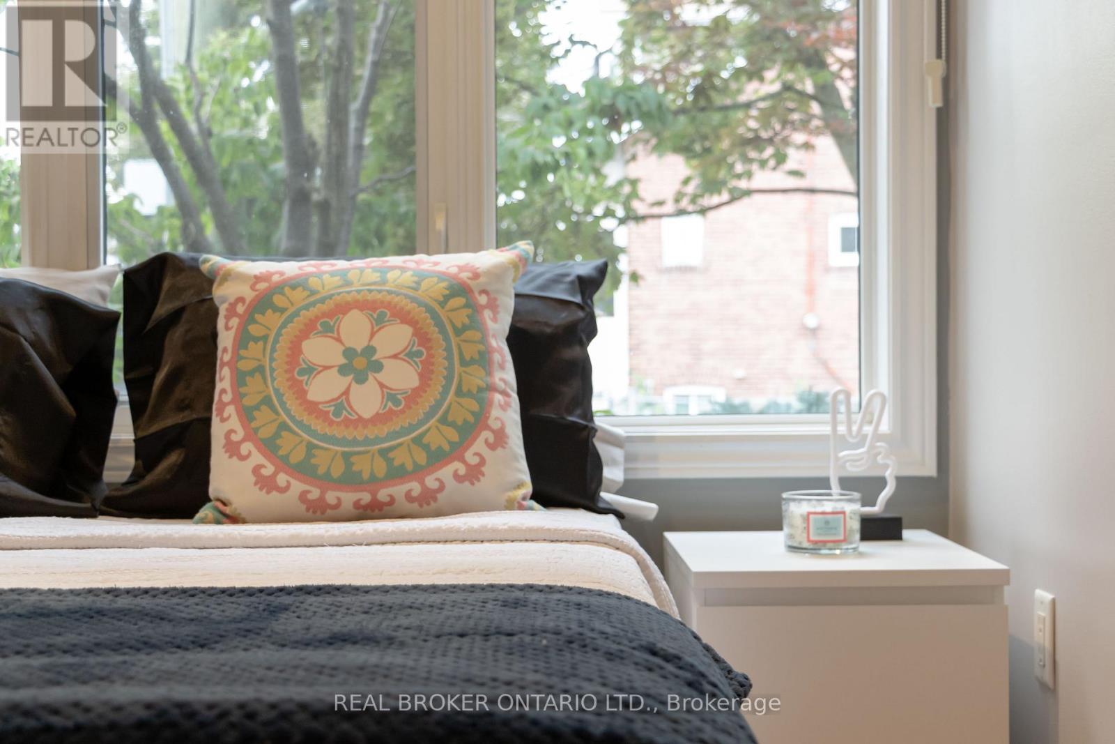 A bedroom with a bed, a window, and a nightstand with a candle on it.