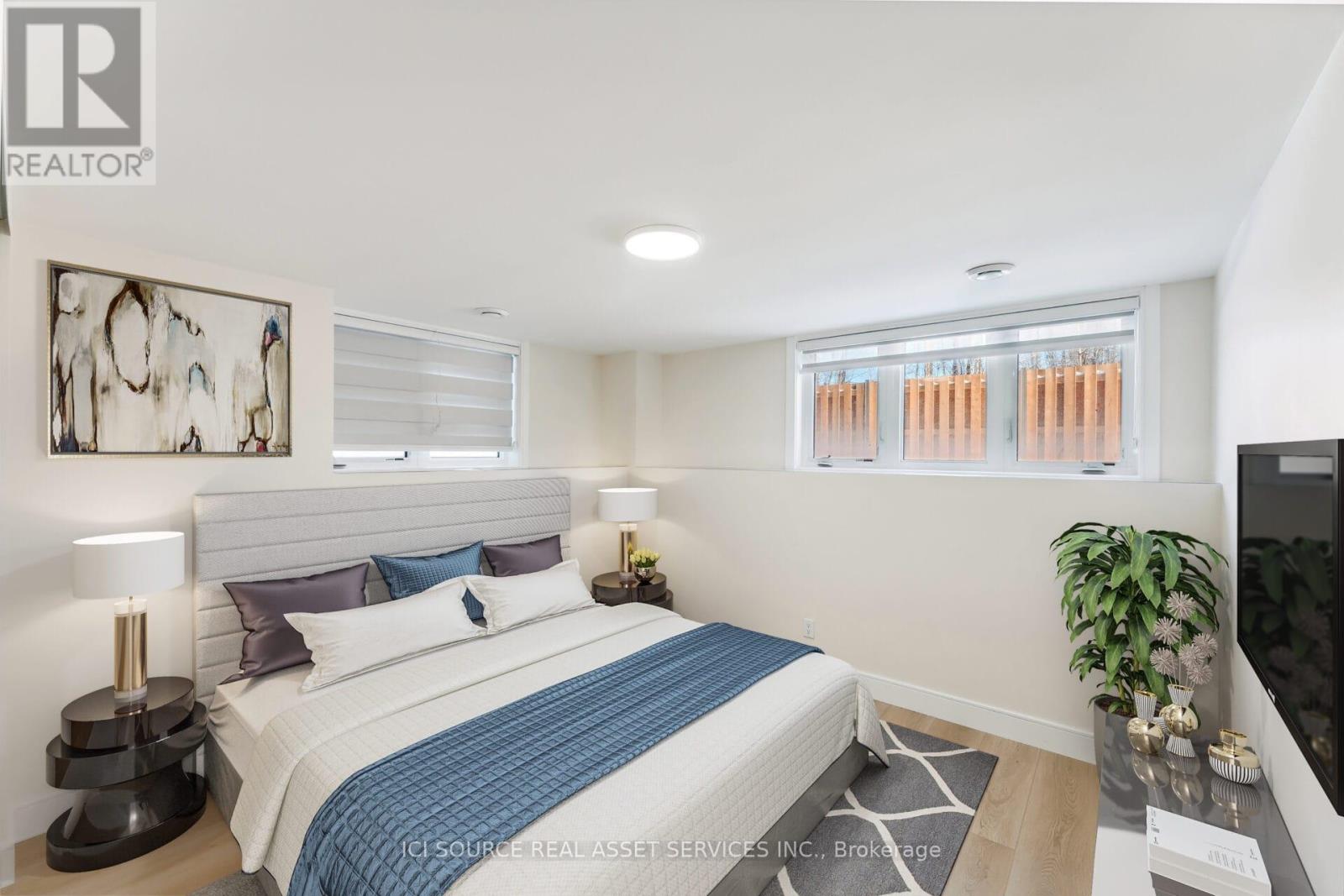 A bedroom with a bed, a lamp, a plant, and a painting on the wall.