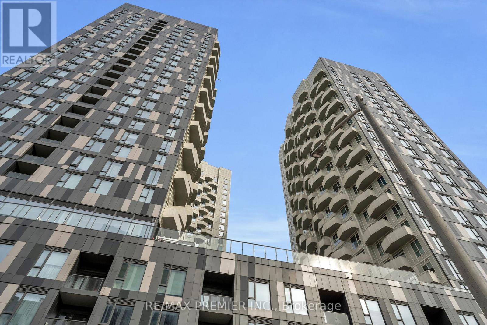 Two tall buildings with balconies and windows are shown under a clear blue sky.