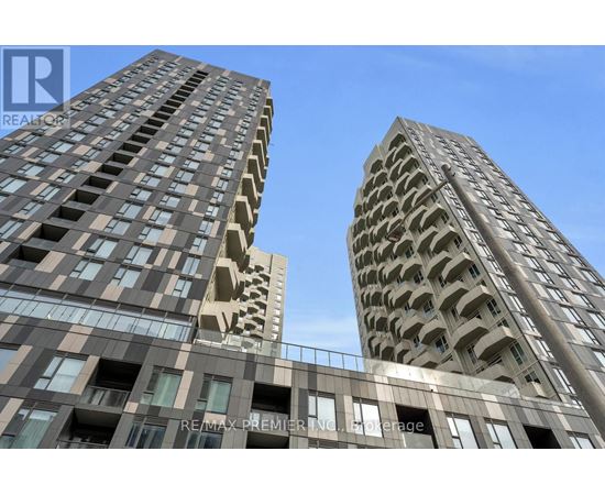 Two tall buildings with balconies and windows are shown under a clear blue sky.