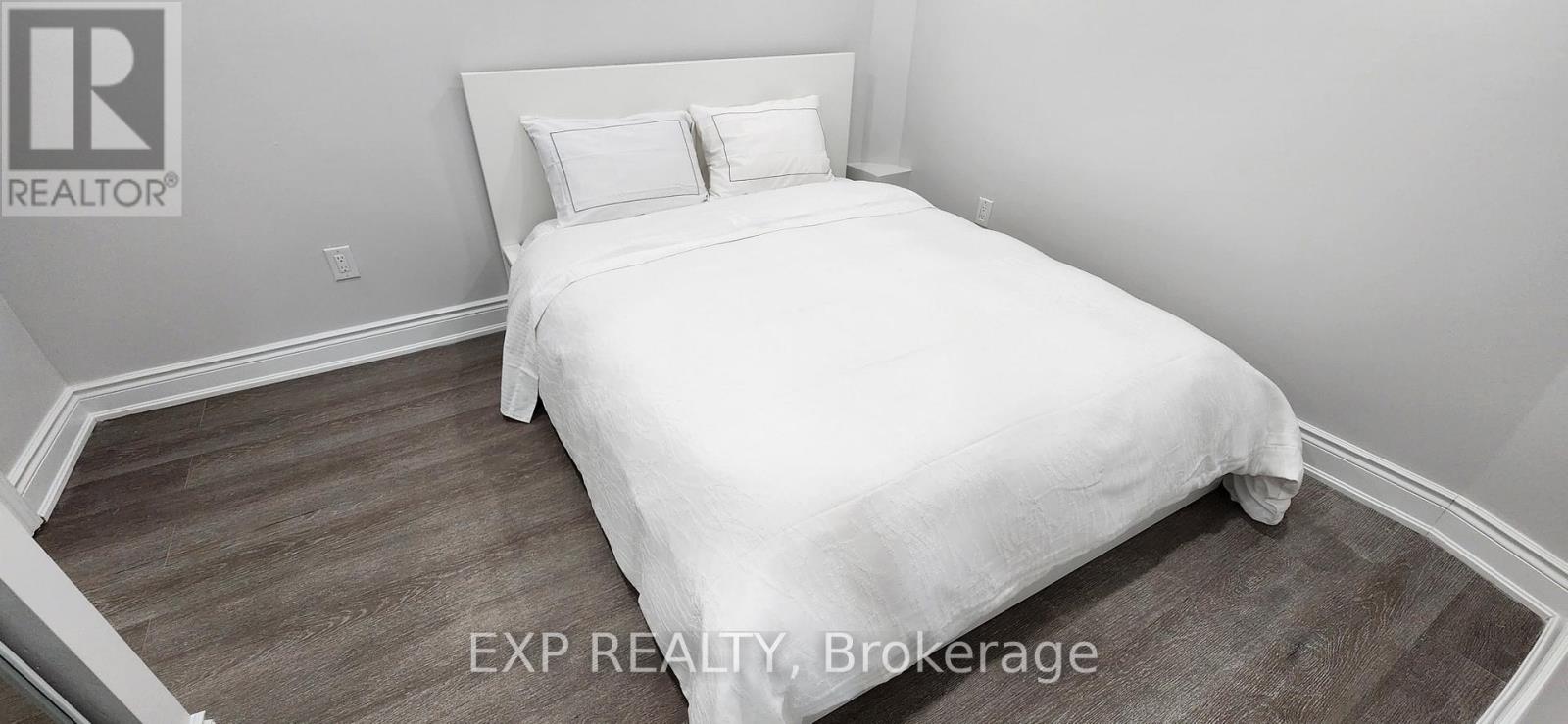 A bedroom with a white bed and wooden flooring.
