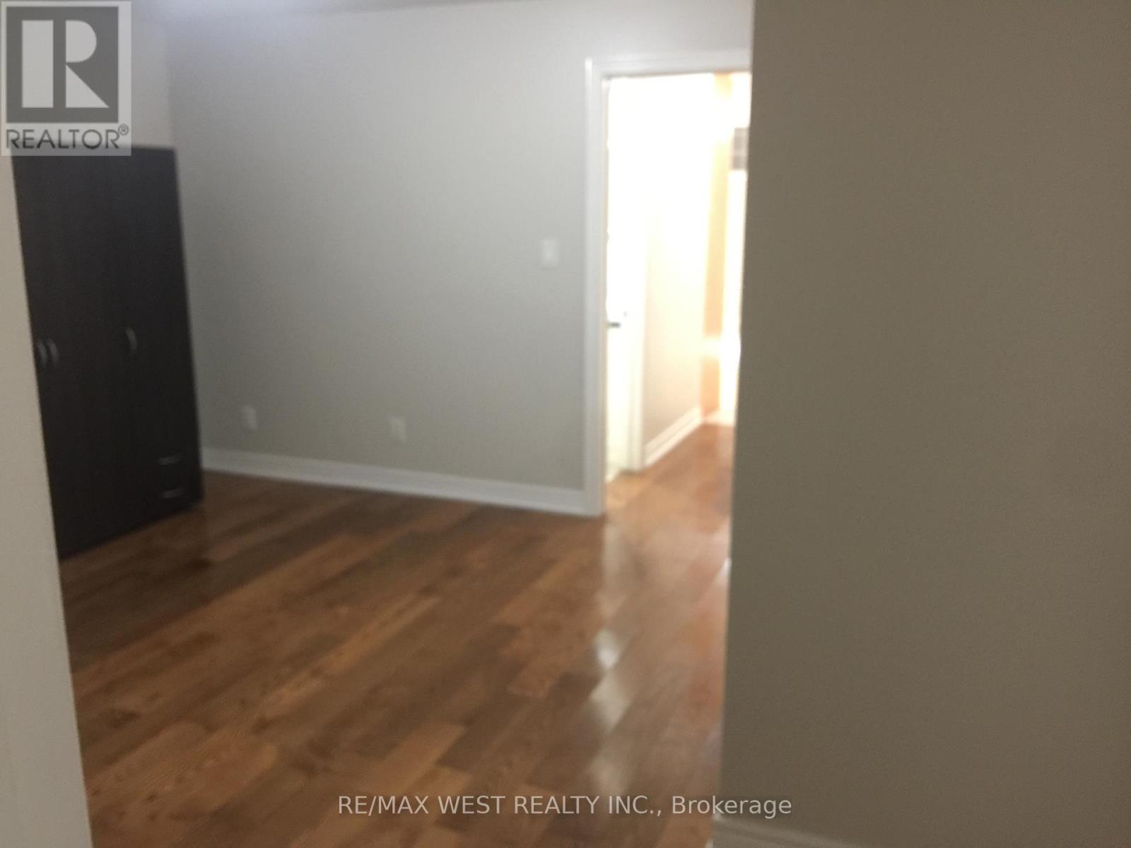 A room with wooden flooring and a white wall with a doorway leading to another room.