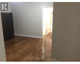 A room with wooden flooring and a white wall with a doorway leading to another room.