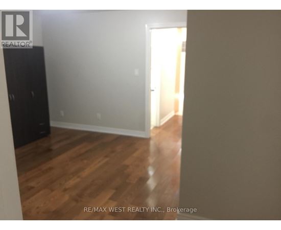 A room with wooden flooring and a white wall with a doorway leading to another room.