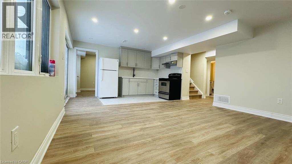 A spacious living area with wood flooring and a kitchen in the background.