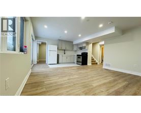 A spacious living area with wood flooring and a kitchen in the background.