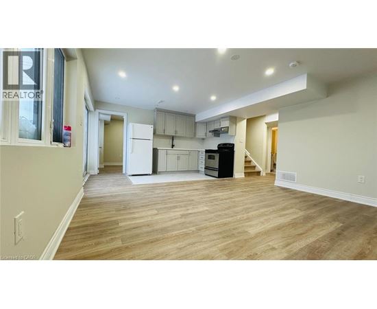 A spacious living area with wood flooring and a kitchen in the background.