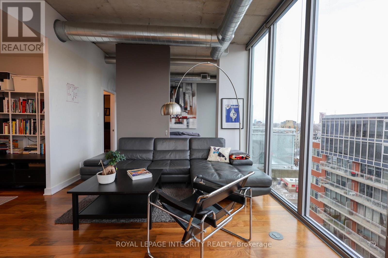A living room with a black leather couch and a coffee table in front of a large window.