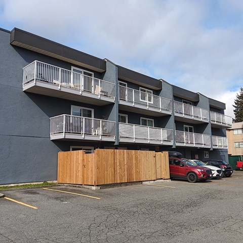 A parking lot with a red car and a building with balconies.