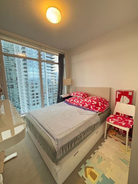 A small child's bedroom with a large window and a white bed.