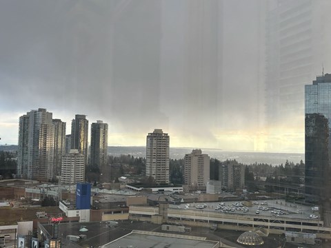 A cityscape with buildings and a parking lot is visible through a window with rain on it.