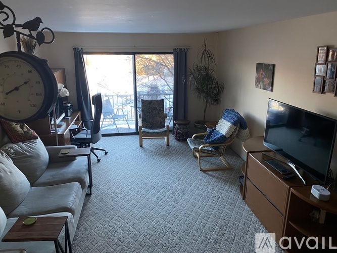 A living room with a grey sofa, a wooden coffee table, a television, and a large window with a view of the outside.