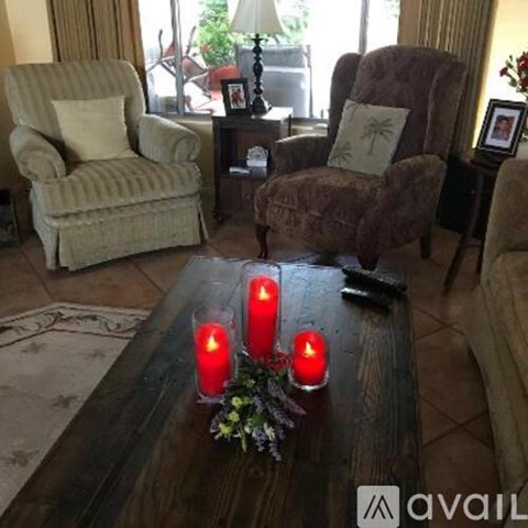 A living room with a brown couch, a chair, and a table with three red candles on it.