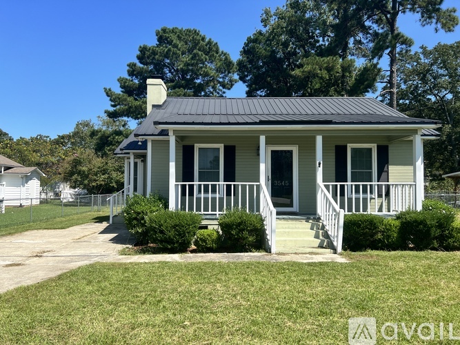 A small house with a porch and a black roof is for sale.
