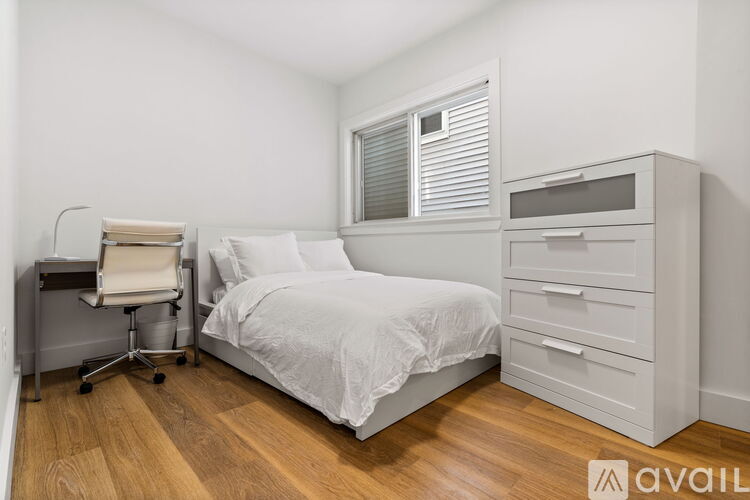 A white bedroom with a bed, chair, and cabinet.