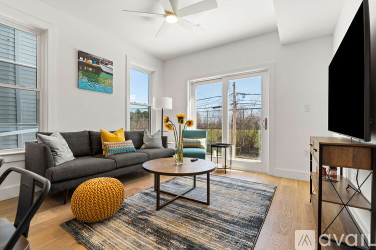 A living room with a grey couch, a yellow pouf, a coffee table, and a television.