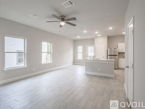 A spacious, empty room with a ceiling fan and a kitchenette in the background.