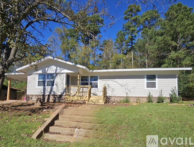 A house with a white exterior and a porch is surrounded by trees.
