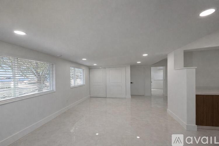 A spacious room with white walls and a large window with blinds.