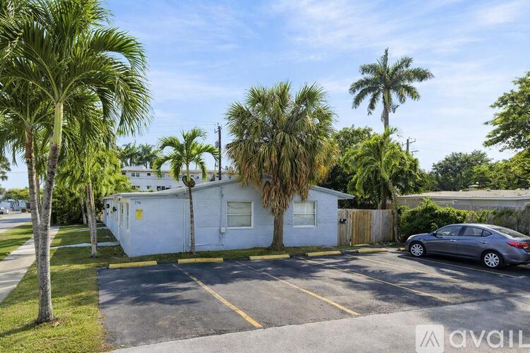 A car is parked in a parking lot with a white building and palm trees in the background.
