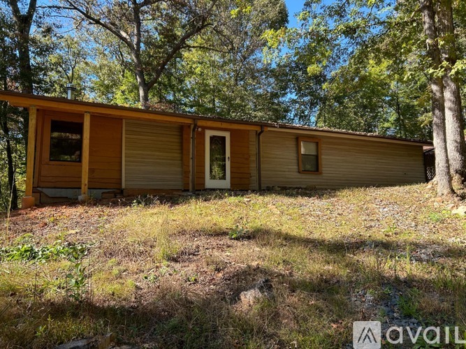 A wooden cabin is situated in a grassy area with trees in the background.