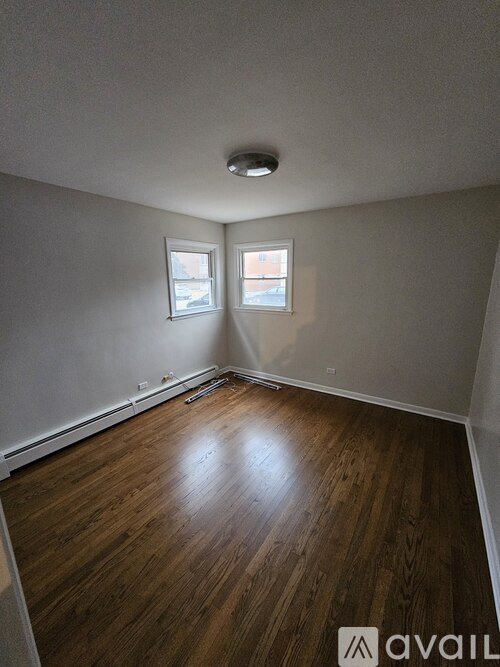 A room with wooden flooring and two windows.