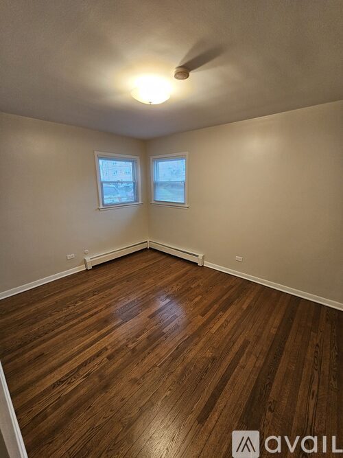 A room with wooden flooring and two windows.