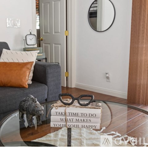A living room with a grey couch, a glass coffee table, and a sign on the table that says "Take time to do what makes your soul happy".