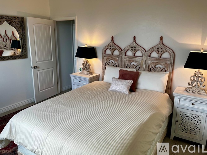 A bedroom with a bed, two lamps, and a mirror.