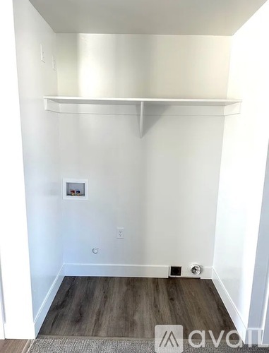A white wall with a shelf and a wooden floor.