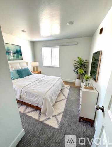 A bedroom with a bed, nightstand, and a plant.
