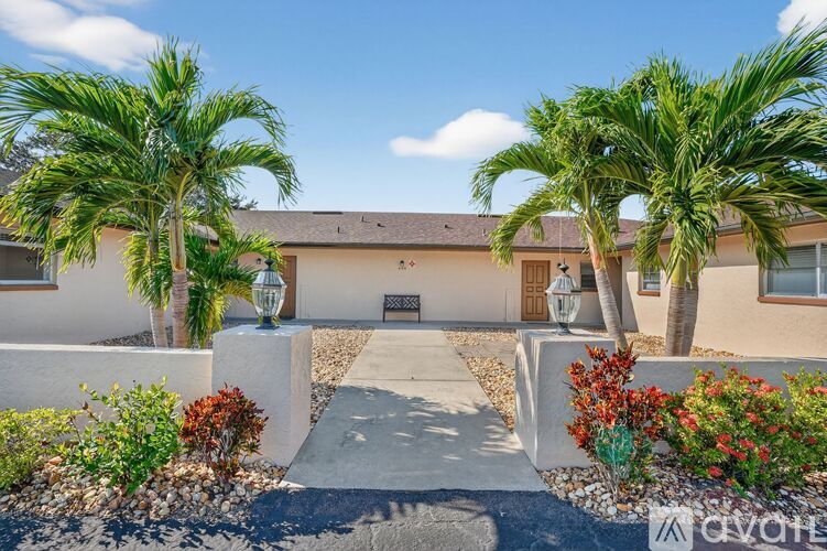 A house with a front yard featuring a concrete pathway, palm trees, and a bench.