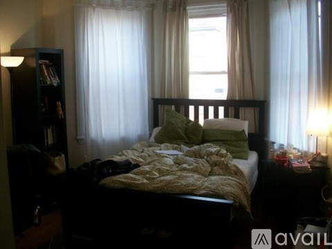 A bedroom with a bed, nightstand, and window with curtains.